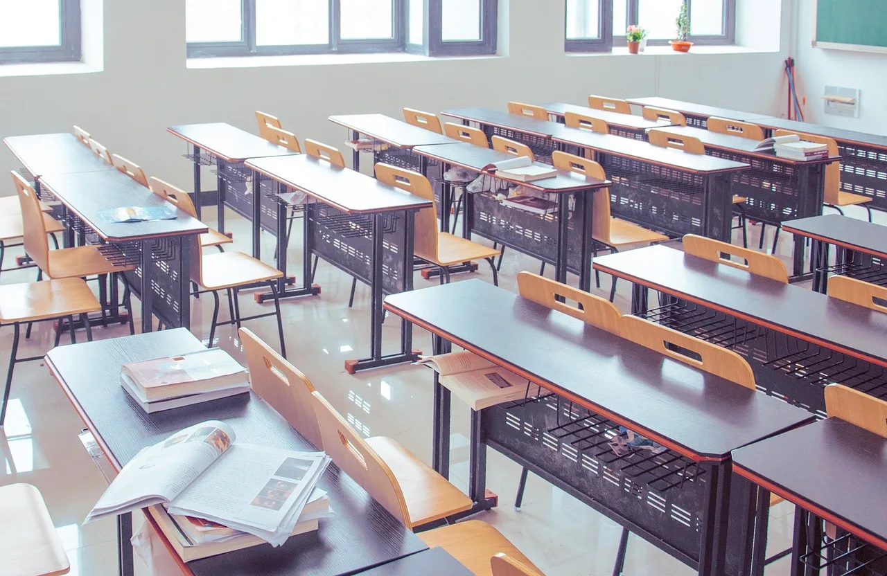 Pusta sala lekcyjna z rzędami ławek i krzeseł ustawionych naprzeciw tablicy, na pierwszych stolikach widoczne podręczniki i materiały edukacyjne. Ujęcie nawiązuje do zorganizowanych zajęć oraz systematycznego przygotowania do matury w Szczecinie – więcej informacji o kursach dostępnych jest na stronie organizatora - Symposio.
